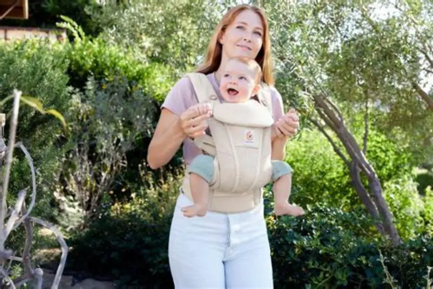 parent wearing newborn in ergonomic baby carrier indoors